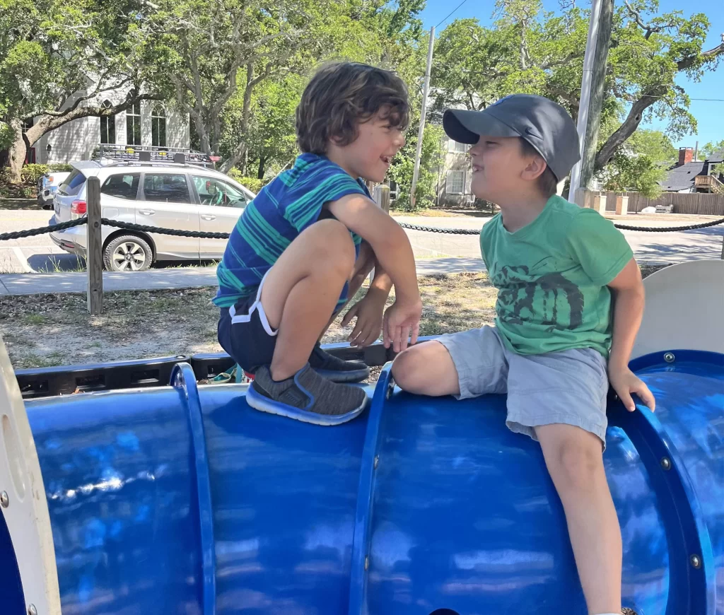 two young boys playing on blue slide outside having fun