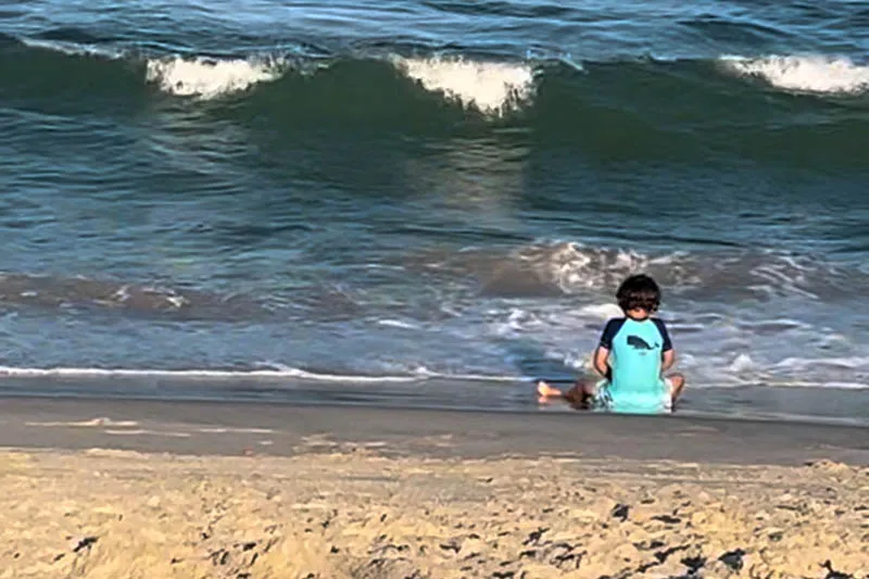 little boy sitting on beach looking at ocean