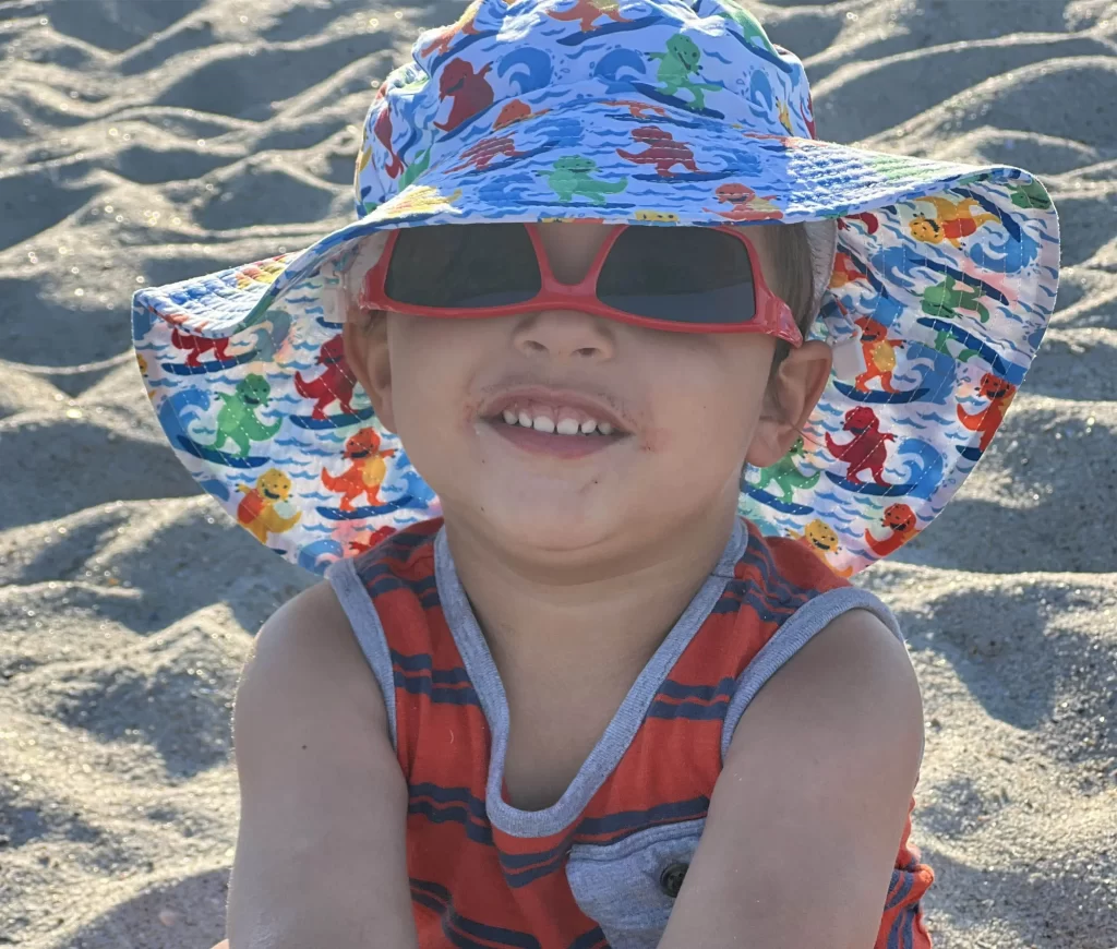 young boy wearing sunglasses and oversized hat on beach