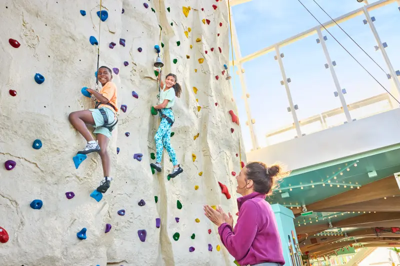 A mom cheering on two children rock climbing on cruise ship.