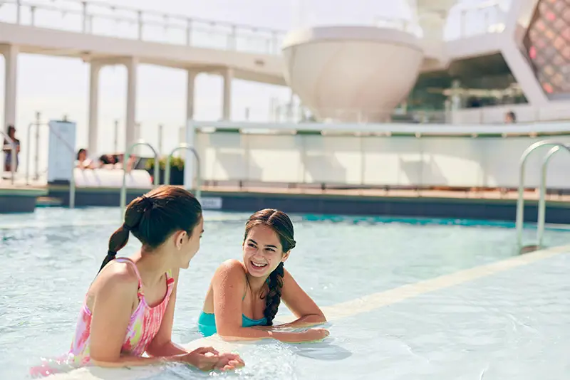 Two teen girls talking by edge of pool on cruise ship.