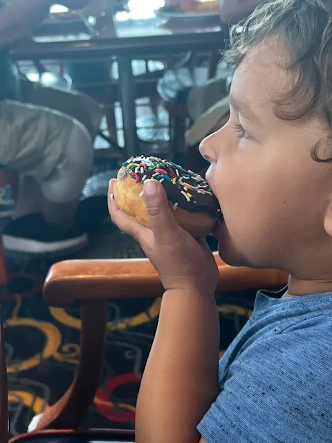 A boy toddler eating a chocolate sprinkle donut side view.