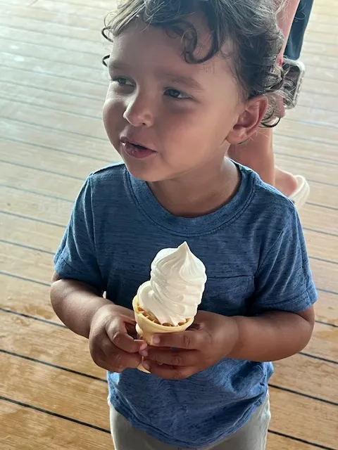 A boy toddler holding a vanilla ice cream cone.