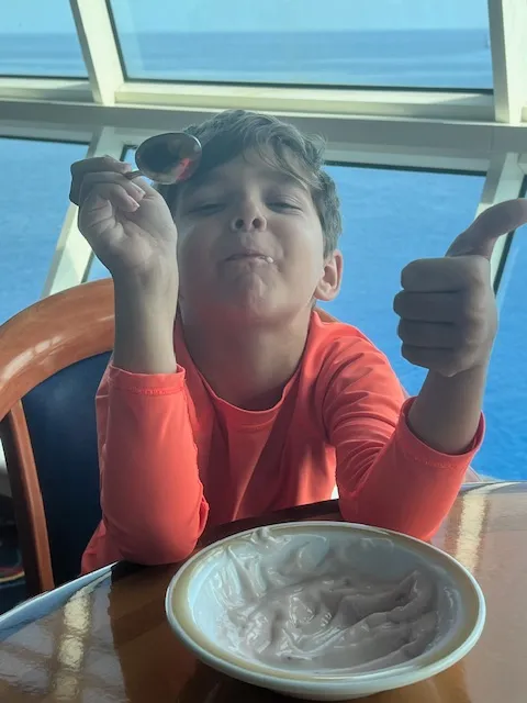 A little boy eating with a smile and a thumbs up.