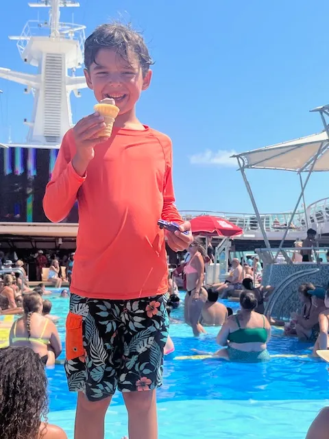 A little boy smiling with ice cream cone in pool on sunny day.