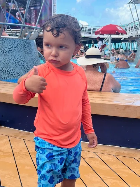 A boy toddler looking off to the side with thumbs up.