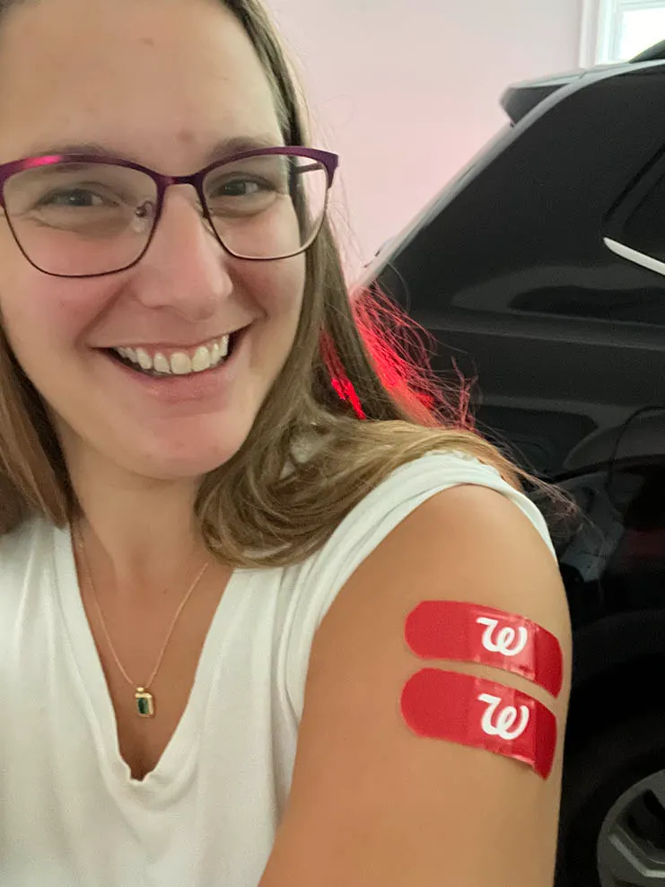 A woman smiling with two red bandages on her arm after getting vaccinated.