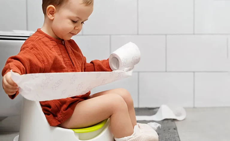 A toddler sitting on toilet with toilet paper roll.