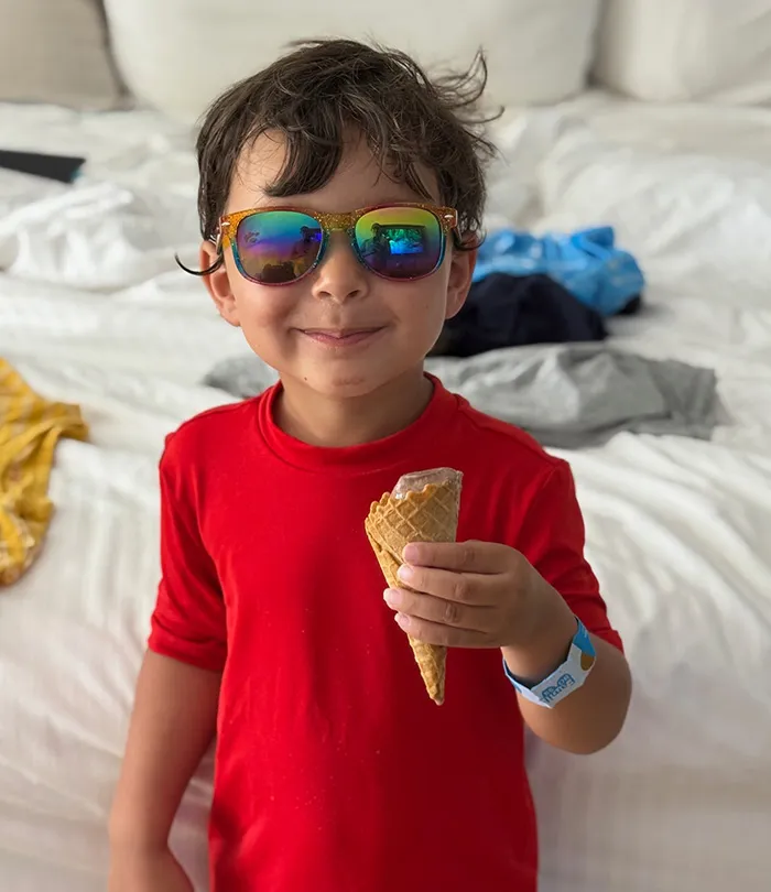 A boy toddler wearing sunglasses and eating an ice cream cone very happy.