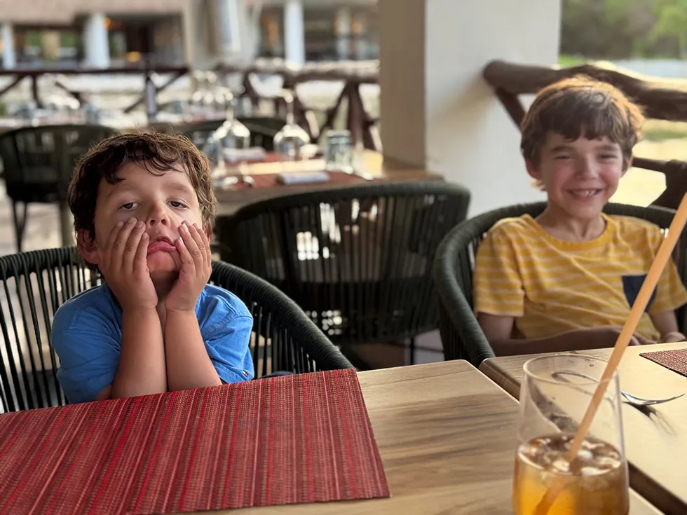 Two happy young boys sitting at a restaurant table outside.