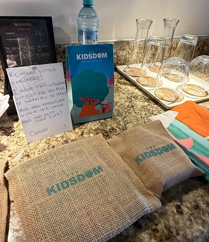 A welcome kit for kids on a granite countertop in hotel room includes a note, a Kidsdom activity book, and burlap bags.