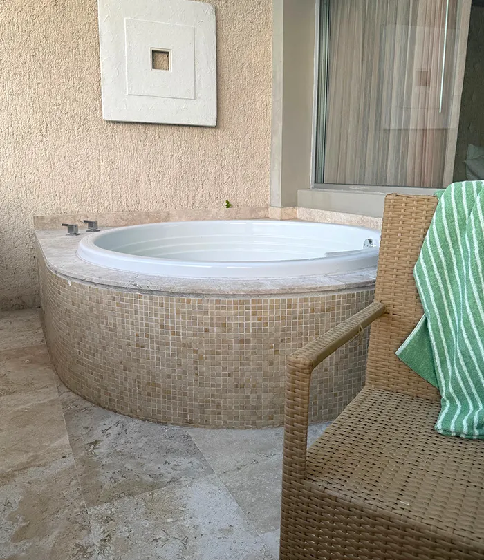 A round, built-in jacuzzi tub with beige mosaic tiles in a corner, not too inviting.
