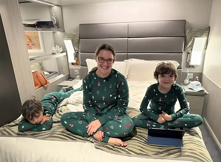 A family in matching Christmas pajamas relaxing on a bed inside their MSC Seashore Yacht Club stateroom during a Christmas family cruise.