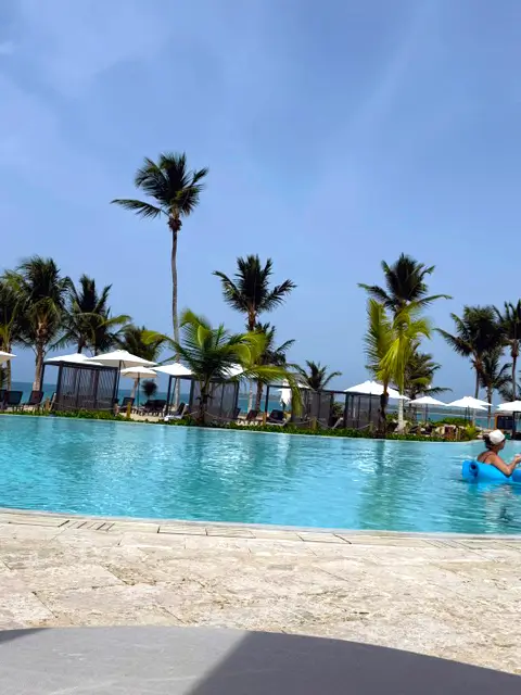 Large outdoor swimming pool lined with palm trees and ocean views at the Secrets Playa Esmeralda resort in Miches.